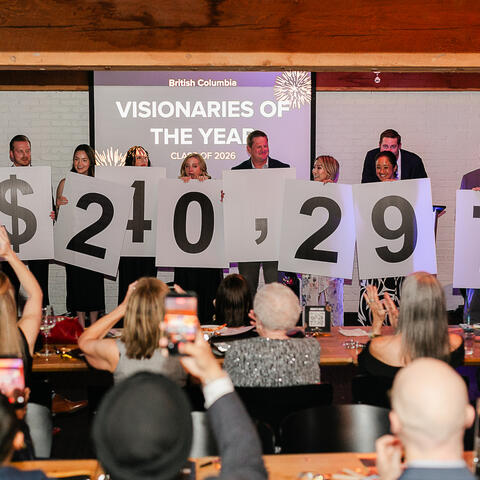 Des participants sur scène brandissent les chiffres de la collecte pendant que les invités applaudissent le total de 240 297 $.