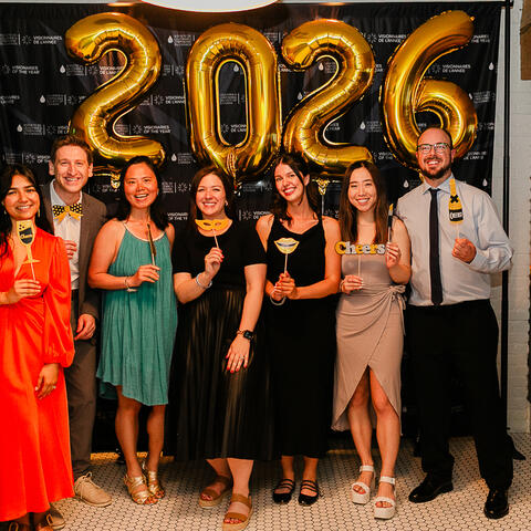 Sept participants posent avec des accessoires amusants près des ballons dorés 2026 lors de la célébration Visionnaires.
