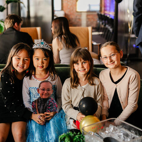 Quatre enfants se reposent ensemble sur un canapé vert entouré de ballons et d’un décor festif pendant le gala.