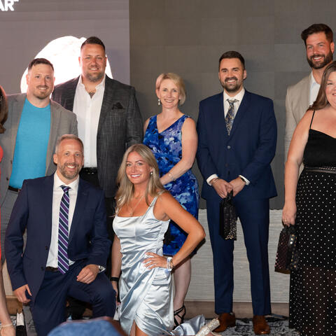 Un groupe de participants pose ensemble sur scène en tenue de soirée pendant la célébration Visionnaires de l’année.