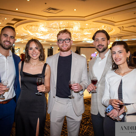 Des participants se rassemblent dans une salle de bal, verre à la main, lors d’un événement-bénéfice animé sous une lumière chaleureuse.