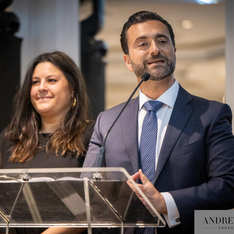 Une personne prend la parole au podium pendant qu’une autre personne se tient à ses côtés sur scène lors d’un événement-bénéfice formel.
