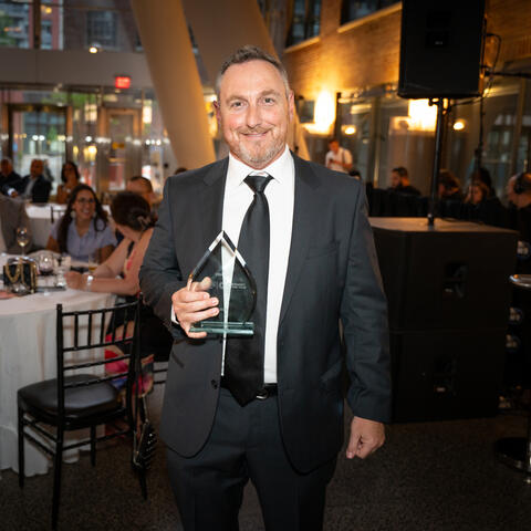 Un participant se tient dans la salle avec un trophée pendant que des invités assis aux tables observent.